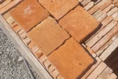 Tomettes carrées orangées disposées à plat sur une caisse de carreaux rangés sur chant.