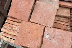 Tomettes carrées rosées présentées à plat au-dessus de carreaux empilés dans une caisse.
