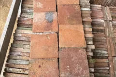 Tomettes carrées rouges et ocre présentées sur une caisse de carreaux rangés sur chant.
