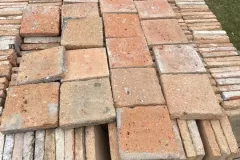 Tomettes carrées aux teintes ocre, beige et rosée présentées sur une caisse de carreaux.